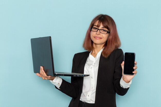 Impiegato di ufficio femminile di vista frontale che tiene smartphone e computer portatile sulla superficie blu