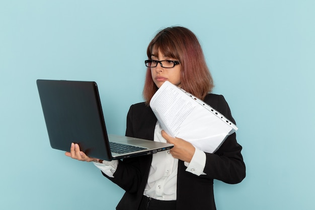 Impiegato di ufficio femminile di vista frontale in vestito rigoroso che tiene documenti e laptop sulla superficie blu