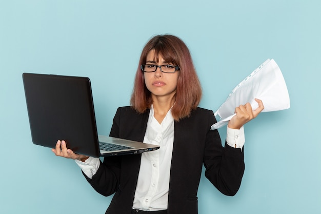 Impiegato di ufficio femminile di vista frontale in vestito rigoroso che tiene documenti e laptop sulla superficie blu