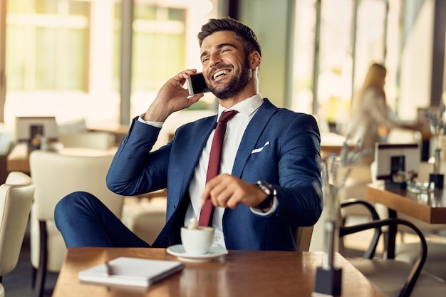 Imprenditore allegro che fa una telefonata mentre beve una tazza di caffè in un bar