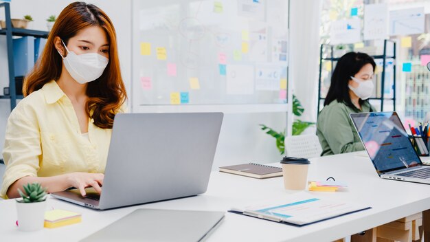 Imprenditore asiatico di uomini d'affari che indossa una maschera medica per l'allontanamento sociale in una nuova situazione normale per la prevenzione dei virus mentre utilizza il laptop al lavoro in ufficio. Stile di vita dopo il virus corona.