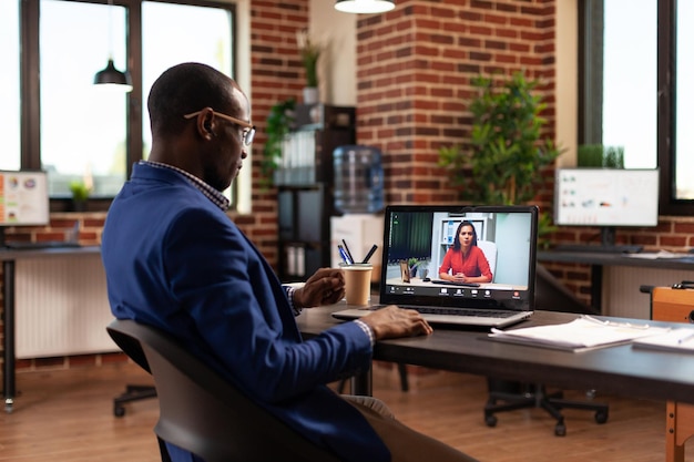 Imprenditore che utilizza una videochiamata online per parlare con una donna sul laptop per la pianificazione del progetto. Uomo d'affari che incontra una persona in videoconferenza remota, conversando sulla strategia.