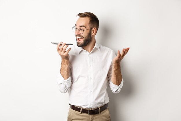 Imprenditore eccitato parlando in vivavoce e sorridente, registrare il messaggio vocale con la faccia estatica, in piedi