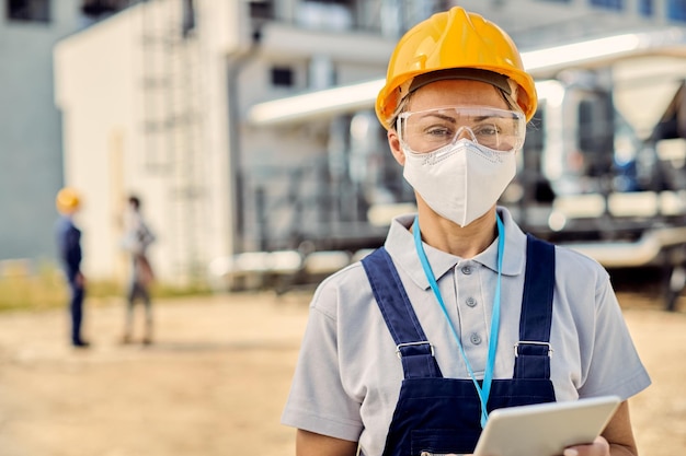 Imprenditore edile femminile con tablet digitale che indossa una maschera facciale in cantiere