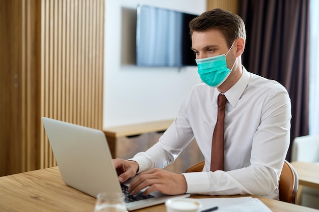 Imprenditore maschio con maschera protettiva che lavora su laptop mentre è in viaggio d'affari