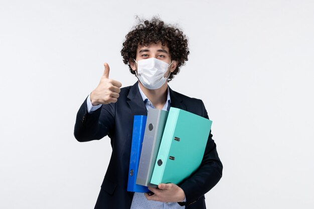 Imprenditore maschio emotivo in tuta e indossa la sua maschera che tiene documenti facendo un gesto ok sulla superficie bianca