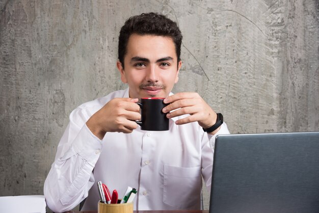 Imprenditore tenendo la tazza di tè alla scrivania in ufficio.