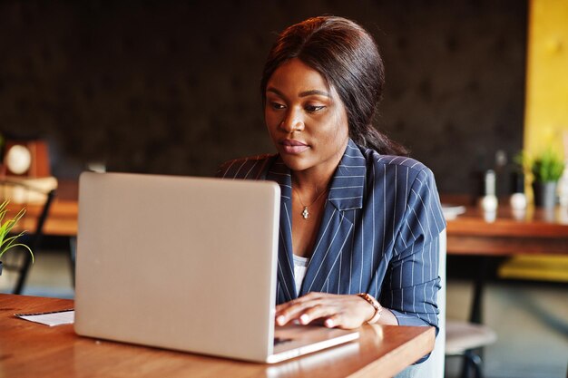 Imprenditrice afroamericana seduta al tavolo in caffè Ragazza nera che lavora con il computer portatile