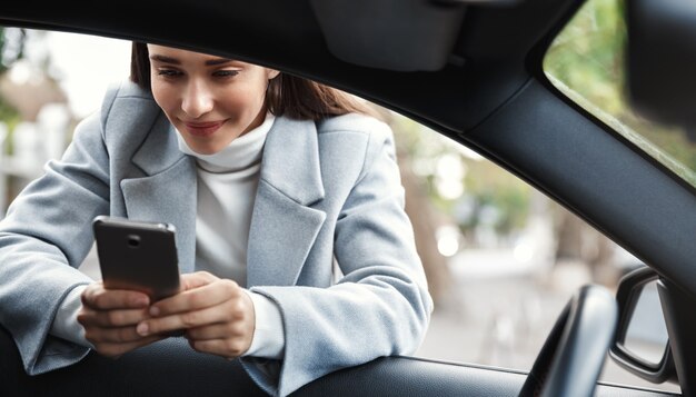 Imprenditrice appoggiato al finestrino della macchina e messaggio di testo sul telefono, sorridendo felice.