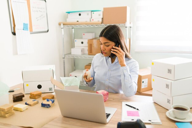 Imprenditrice e imprenditrice che parla al telefono con un cliente mentre prepara pacchetti con prodotti di bellezza naturali da spedire