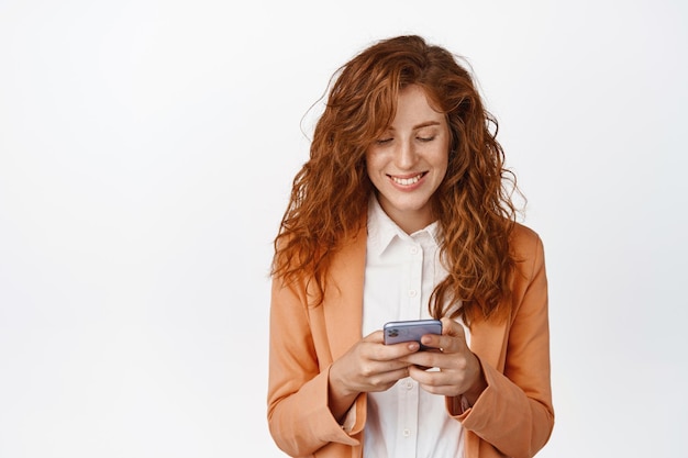 Imprenditrice in chat sul telefono cellulare che indossa la tuta Operaia d'ufficio che utilizza lo smartphone sorridente mentre guarda lo sfondo bianco dello schermo