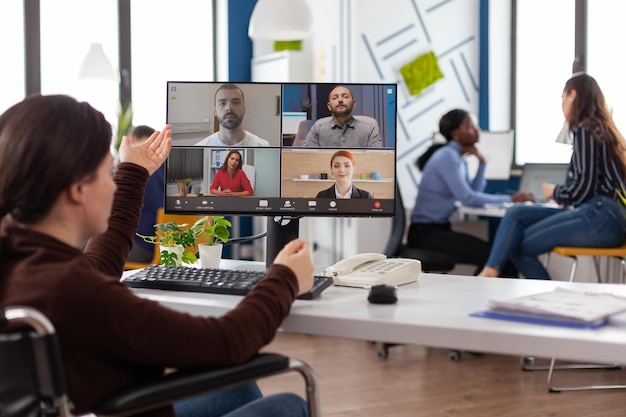 Imprenditrice paralizzata in sedia a rotelle che discute la strategia di marketing con il team remoto durante la conferenza videochiamata online in ufficio commerciale. Teleconferenza sullo schermo del computer