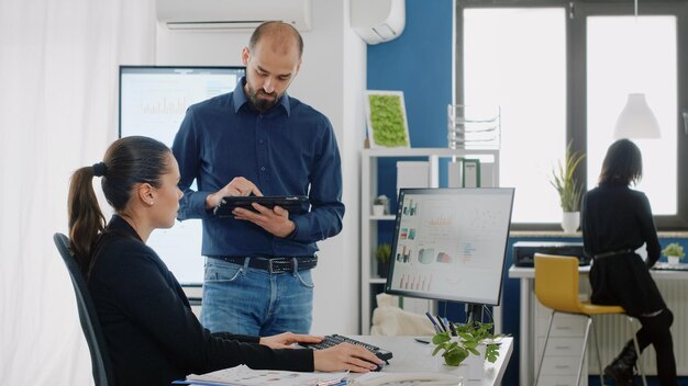 Imprenditrice parlando con l'uomo con tablet digitale sulla pianificazione del progetto e la strategia di marketing. Donna che fa lavoro di squadra con un ingegnere per la progettazione di presentazioni con grafici di dati sul computer