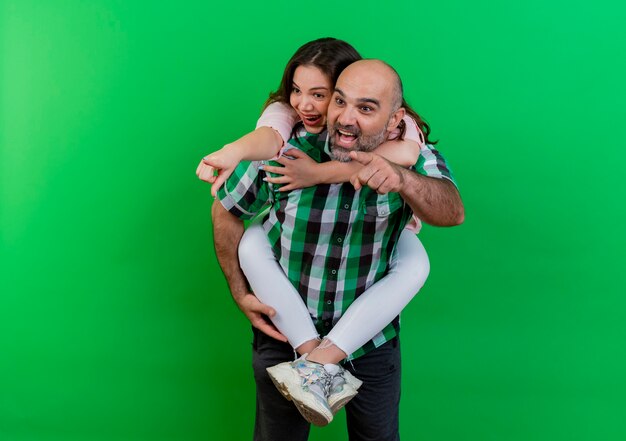 Impressionato coppia adulta uomo che tiene la donna sulla schiena sia guardando che indicando il lato isolato sulla parete verde con lo spazio della copia
