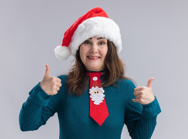 Impressionato donna caucasica adulta con cappello da Babbo Natale e santa cravatta pollici in su isolato sul muro bianco con copia spazio