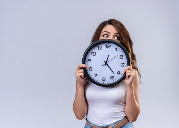 Impressionato giovane bella ragazza che tiene l'orologio e nascondersi dietro di esso guardando il lato destro con lo spazio della copia