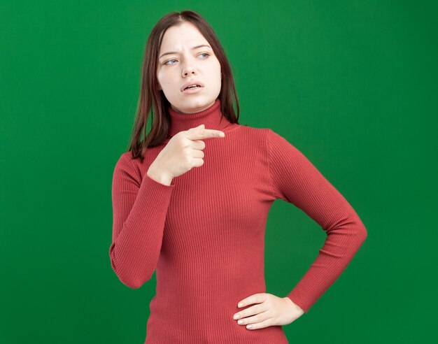 Impressionato giovane bella ragazza che tiene la mano sulla vita guardando e indicando il lato