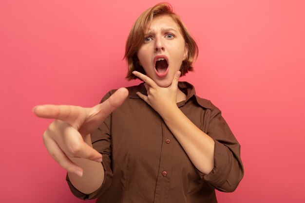 Impressionato giovane donna bionda che guarda e indica il mento davanti tenendo premuto