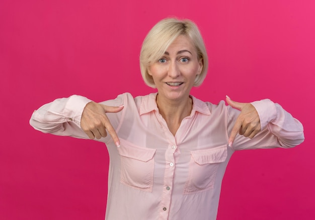 Impressionato giovane donna bionda slava rivolta verso il basso isolato su sfondo rosa