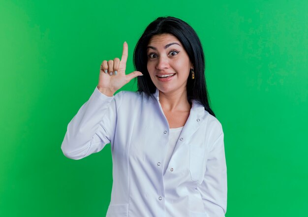 Impressionato giovane medico femminile che indossa abito medico guardando facendo gesto perdente