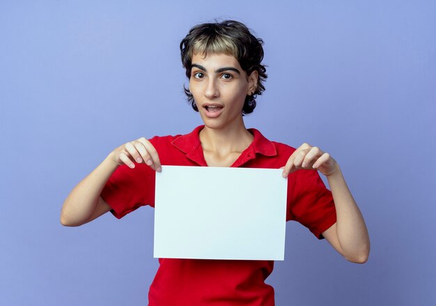 Impressionato giovane ragazza caucasica con pixie haircut holding appunti isolati su sfondo viola