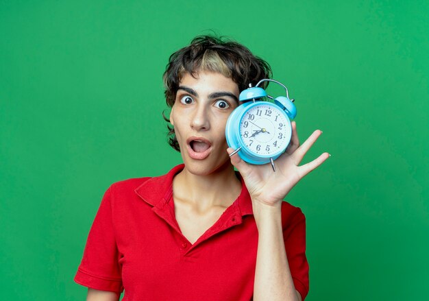 Impressionato giovane ragazza caucasica con taglio di capelli pixie che tiene sveglia isolata su priorità bassa verde