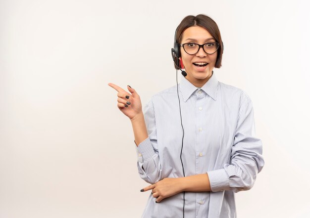 Impressionato giovane ragazza della call center con gli occhiali e auricolare rivolto verso il lato isolato su bianco con spazio di copia