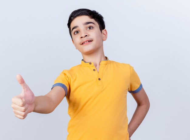 Impressionato giovane ragazzo caucasico tenendo la mano sulla vita guardando dritto mostrando pollice in alto isolato su sfondo bianco con spazio di copia