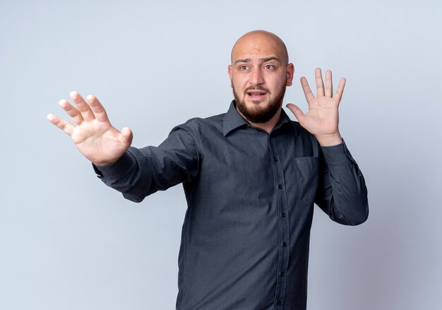 Impressionato giovane uomo calvo della call center che guarda al lato che mostra la mano vuota e allunga la mano sul lato che non fa gesticolare isolato su bianco