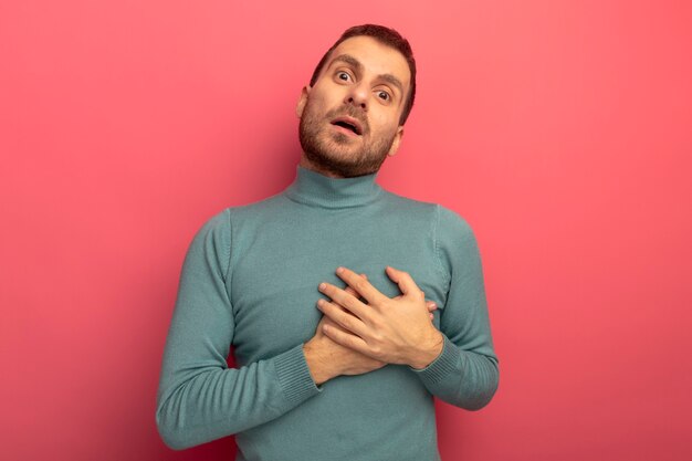 Impressionato giovane uomo caucasico che guarda l'obbiettivo mettendo le mani sul cuore isolato su sfondo cremisi con lo spazio della copia