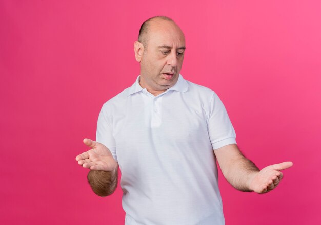 Impressionato imprenditore maturo casual guardando le mani fingere di tenere qualcosa di isolato su sfondo rosa con spazio di copia