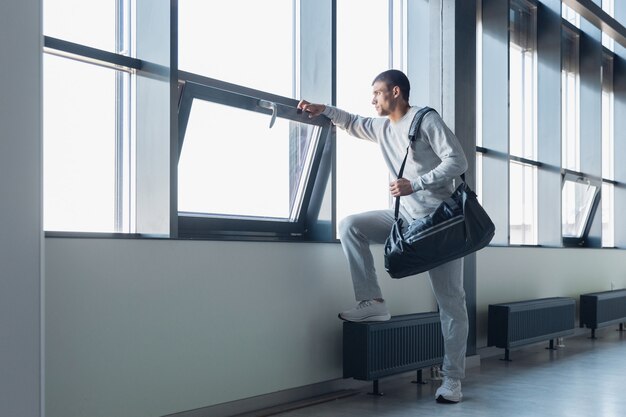 In attesa del cancello. Sportivo che cammina in un moderno edificio a vetri, aeroporto di megapolis. Prima del volo per la competizione. Atleta professionista elegante e sicuro di sé. Viaggio, vacanza, stile di vita sportivo.