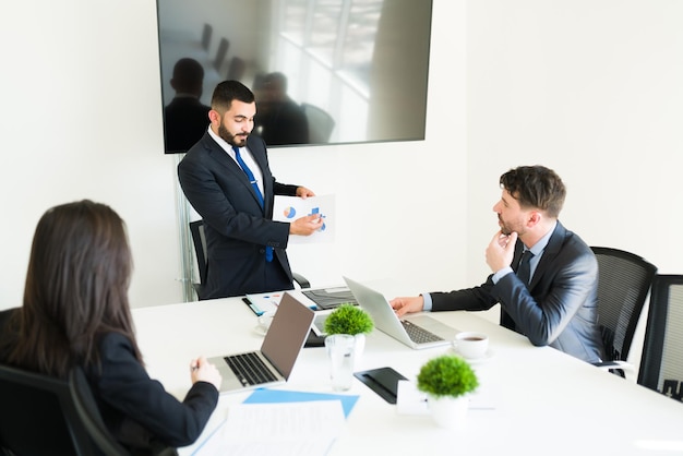 In azienda crescono le vendite. Rappresentante di vendita attraente che mostra un grafico con gli obiettivi aziendali ai suoi colleghi nella sala riunioni