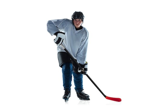 In esecuzione. Giovane giocatore di hockey maschio con il bastone sul campo di ghiaccio e sfondo bianco. Sportivo che indossa attrezzatura e casco che pratica. Concetto di sport, stile di vita sano, movimento, movimento, azione.