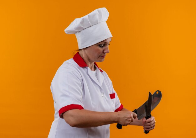 In piedi nella vista di profilo femmina di mezza età cuoco in uniforme da chef tagliente coltello