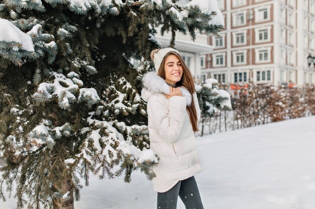 Incantevole donna bionda in giacca bianca e jeans neri in posa durante la passeggiata a winter park. Foto all'aperto di una donna abbastanza alla moda divertendosi nella mattina di dicembre.