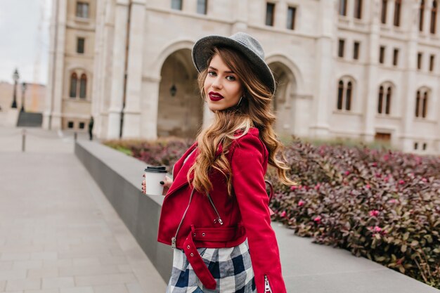 Incantevole giovane donna con acconciatura ondulata guardando sopra la spalla mentre si cammina per la città europea