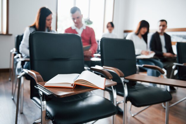 Incentrato sul libro. Gruppo di persone alla conferenza di lavoro in aula moderna durante il giorno