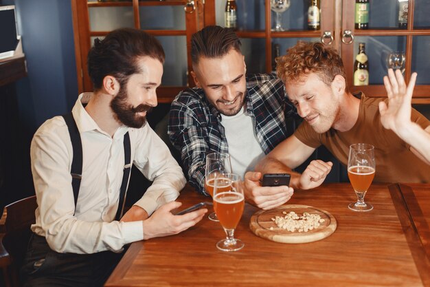 Incontro con i migliori amici. Tre giovani uomini felici in abbigliamento casual a parlare e bere birra seduti insieme al bar.