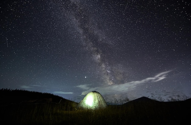 Incredibile cielo stellato in montagna e tenda illuminata al campeggio