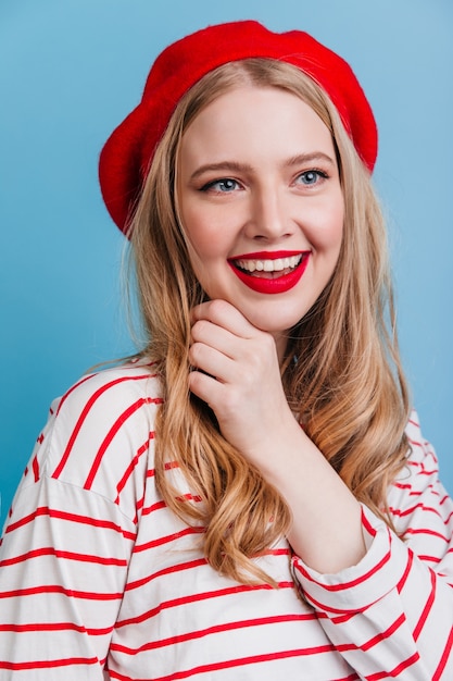 Incredibile donna bionda che esprime emozioni positive. ragazza alla moda in berretto francese sulla parete blu.