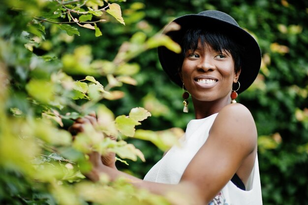 Incredibile donna modello afroamericano in pantaloni verdi e cappello nero in posa al parco