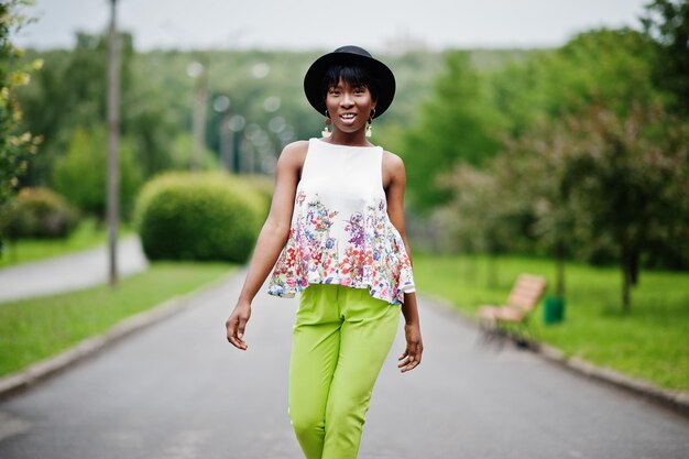 Incredibile donna modello afroamericano in pantaloni verdi e cappello nero in posa con diverse emozioni al parco
