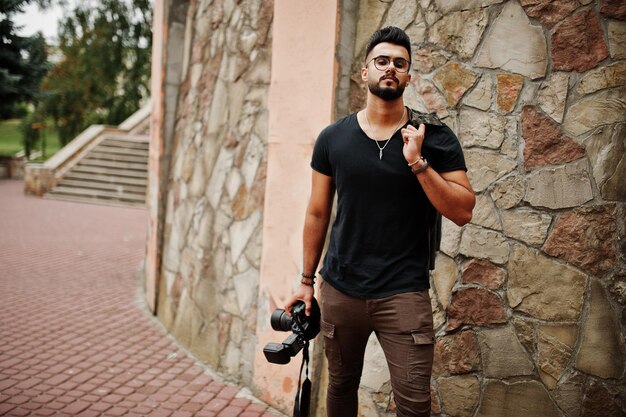 Incredibile fotografo uomo macho con barba araba alta con occhiali e maglietta nera con fotocamera professionale a portata di mano