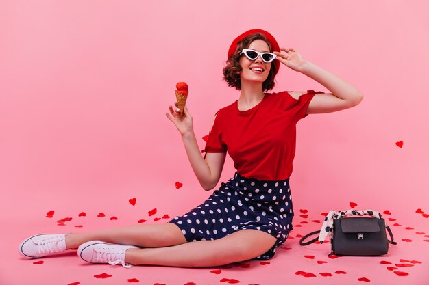 Incredibile ragazza sottile in gonna che mangia il gelato. Adorabile donna caucasica seduta sul pavimento e godersi il dessert.