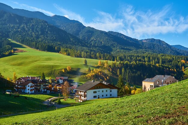 Incredibile scenario autunnale nel villaggio di Santa Maddalena con alberi colorati della chiesa e prati sotto i raggi del sole nascente Alpi Dolomitiche Italia