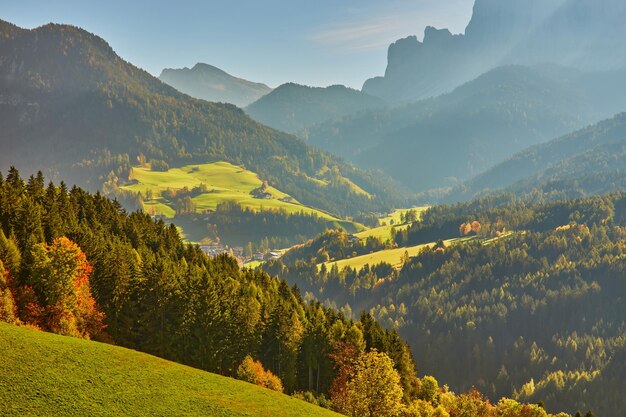 Incredibile scenario autunnale nel villaggio di Santa Maddalena con alberi colorati della chiesa e prati sotto i raggi del sole nascente Alpi Dolomitiche Italia