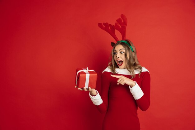 Indicando con regalo. Concetto di Natale, Capodanno 2021, umore invernale, vacanze. . Bella donna caucasica con i capelli lunghi come la confezione regalo di cattura delle renne di Babbo Natale.