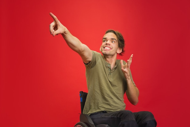 Indicando il giovane disabile caucasico mans ritratto isolato sulla parete rossa dello studio