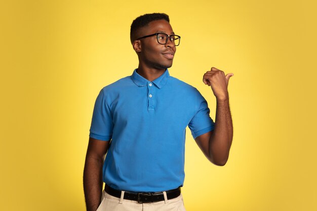 Indicare, mostrare. Ritratto di giovane uomo afro-americano isolato su sfondo giallo studio, espressione facciale. Bellissimo ritratto maschile con copyspace. Concetto di emozioni umane, espressione facciale.